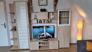 Un salon moderne avec un meuble de rangement en bois pour l’équipement audiovisuel, un téléviseur à écran plat et une table basse en verre.