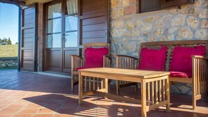 Ein Holztisch und zwei Holzstühle mit roten Kissen auf einer gefliesten Terrasse.