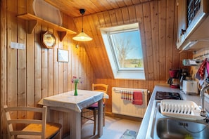 A wooden interior with a dining table, chairs, a window, a radiator, and a kitchen area with a sink and appliances. - Family/child-friendly, lounge with billiards and balcony, free WLAN (Herrnhut OT Ruppersdorf)