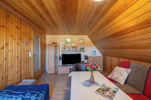 A wooden interior with a TV, sofa, and a table with a vase.