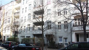 Ein mehrstöckiges Wohngebäude mit Balkonen, parkenden Autos und kahl stehenden Bäumen.
