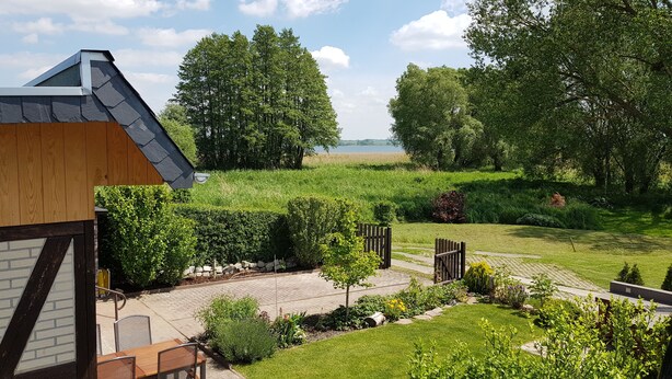 Ein angelegter Garten mit einem gepflasterten Weg, einem Holzzaun und Blick auf einen See.
