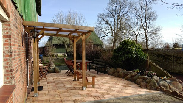 Un patio con mobili in legno, una pergola e un muro in mattoni.