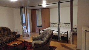 Una camera da letto con un letto a baldacchino, un angolo salotto con divano e poltrona, e un piccolo tavolino con un telecomando.