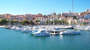 Uma marina com vários barcos atracados, rodeada por edifícios com telhados vermelhos e um céu azul límpido.
