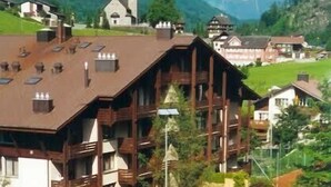 Ein großes Holzgebäude mit mehreren Balkonen, einem Tennisplatz und Blick auf die Berge.