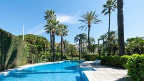 A swimming pool surrounded by palm trees and greenery, with a clear blue sky. - 4 *, BEACH / EVENTS, direct access to the beach, pool, garage, park. (Cannes)