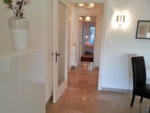 A hallway with a white door, a potted plant, a black chair, and a light fixture on the wall.