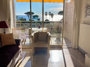 Quarto com sofá, poltrona e vista para o mar através de grandes janelas.