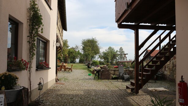 A courtyard with cobblestone flooring, a wooden staircase, and outdoor seating. - Brunow vacation apartment "At home in nature" (Neundorf)