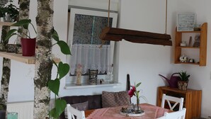 A dining area with a wooden table and white chairs, surrounded by shelves with plants and kitchen items. - Brunow vacation apartment "At home in nature" (Neundorf)