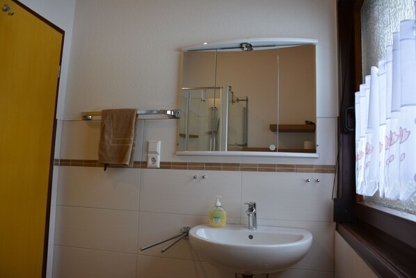 A bathroom with a sink, mirror, towel rack, and shower area.