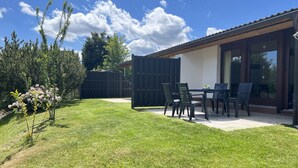 Un patio con mesa y sillas, cerca de madera y césped.
