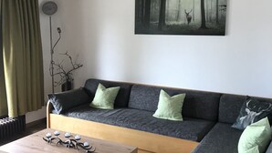 Una sala de estar moderna con un sofá, una mesa de centro y un cuadro que representa un paisaje forestal.