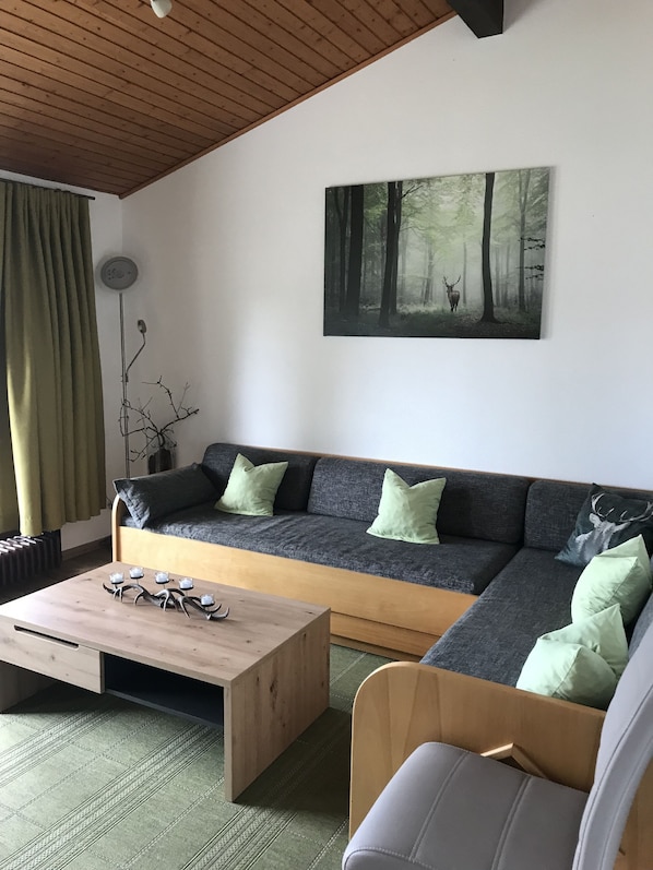A modern living room with a sofa, a coffee table, and a painting of a forest scene.