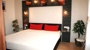 A modern bedroom with a large bed, red pillows, a stone accent wall, and wall-mounted lights. - Comfortable vacation apartment in Zempin - beach vacation on Usedom with your dog (Zempin)