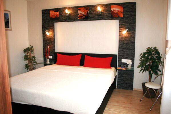 A modern bedroom with a large bed, red pillows, a stone accent wall, and wall-mounted lights.