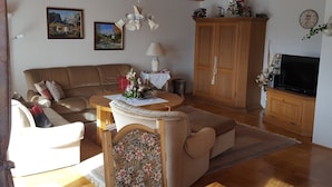 Una sala de estar acogedora con un sofá, un sillón floral, un aparador de madera y un televisor.