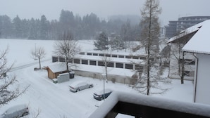 Paisaje nevado con un estacionamiento, un edificio pequeño y una hilera de árboles.