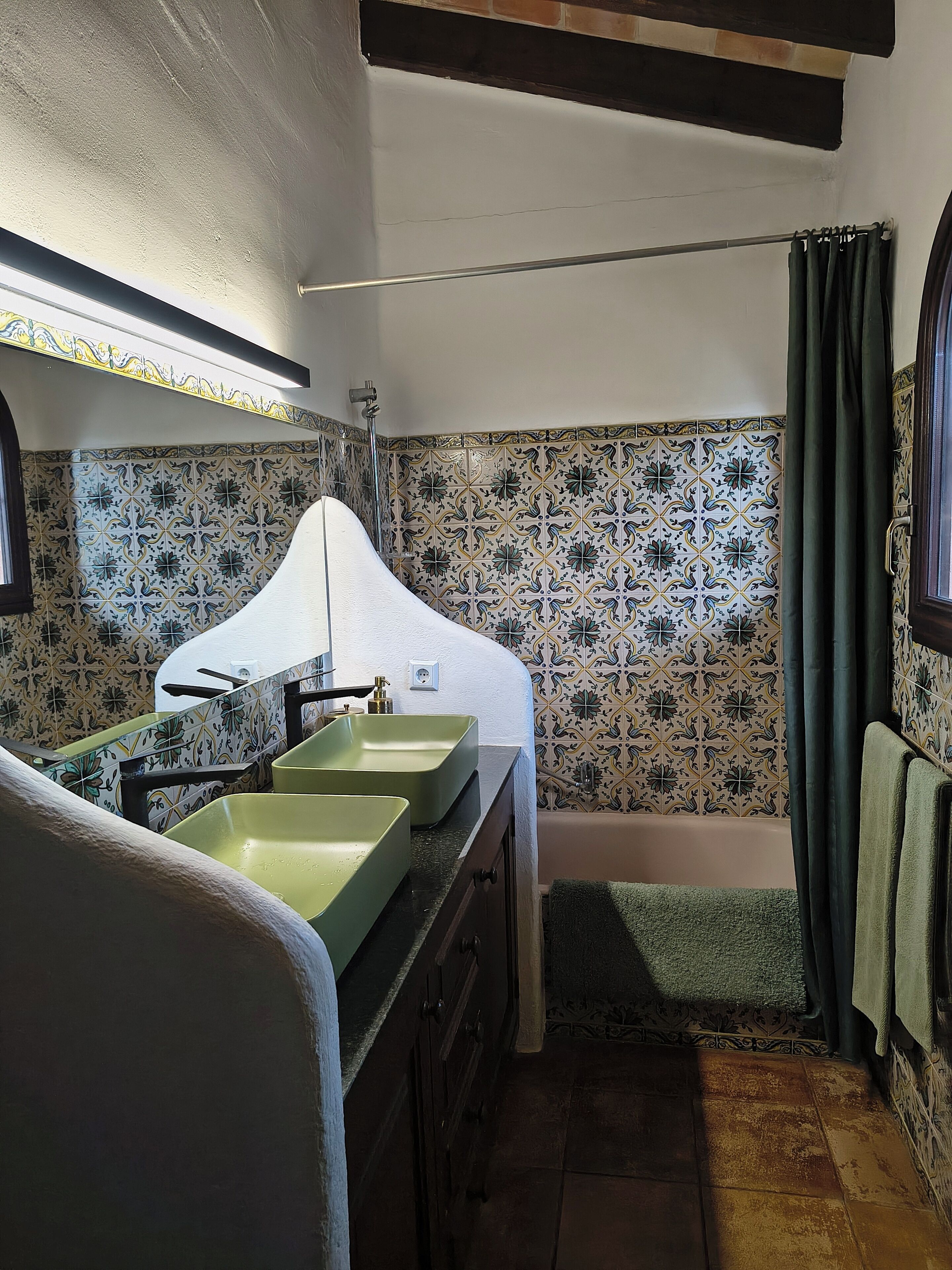 Une petite salle de bain avec deux lavabos verts, une baignoire et une douche. Les murs sont recouverts de carreaux à motifs floraux.