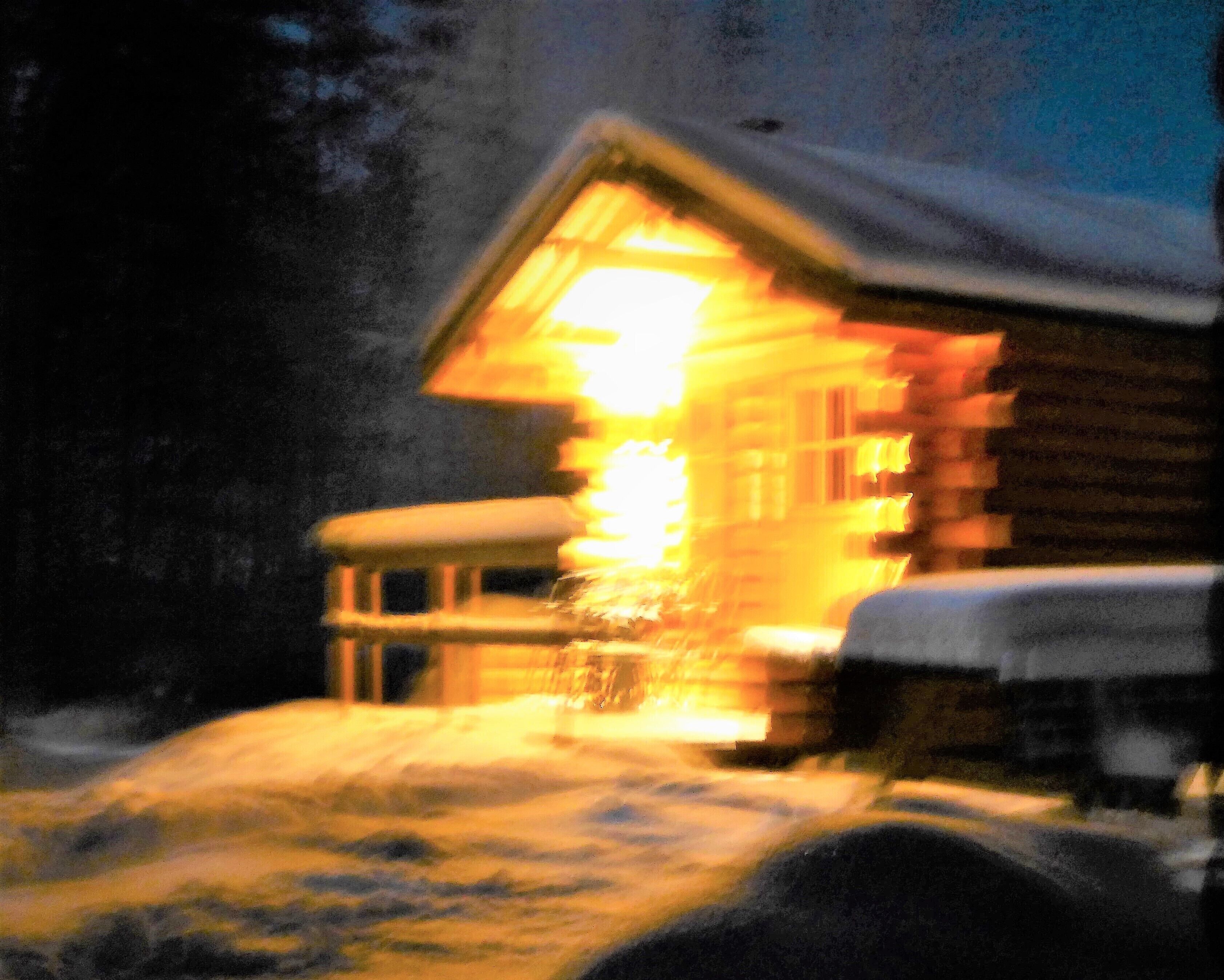 A wooden cabin with a lit interior, surrounded by snow.