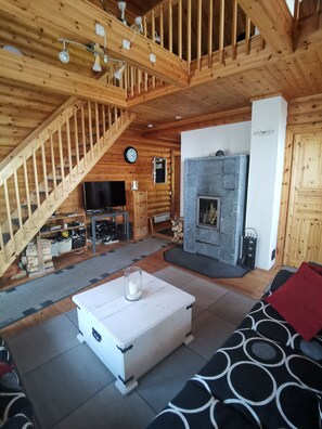 Hirsihirrestä rakennetun mökin sisätilat: kivitakka, puinen portaikko ja televisio.