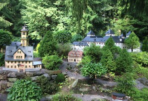 Ein Modell eines Dorfes mit mehreren Gebäuden, darunter eine Kirche mit einem Glockenturm, umgeben von dichtem Grün und Bäumen.