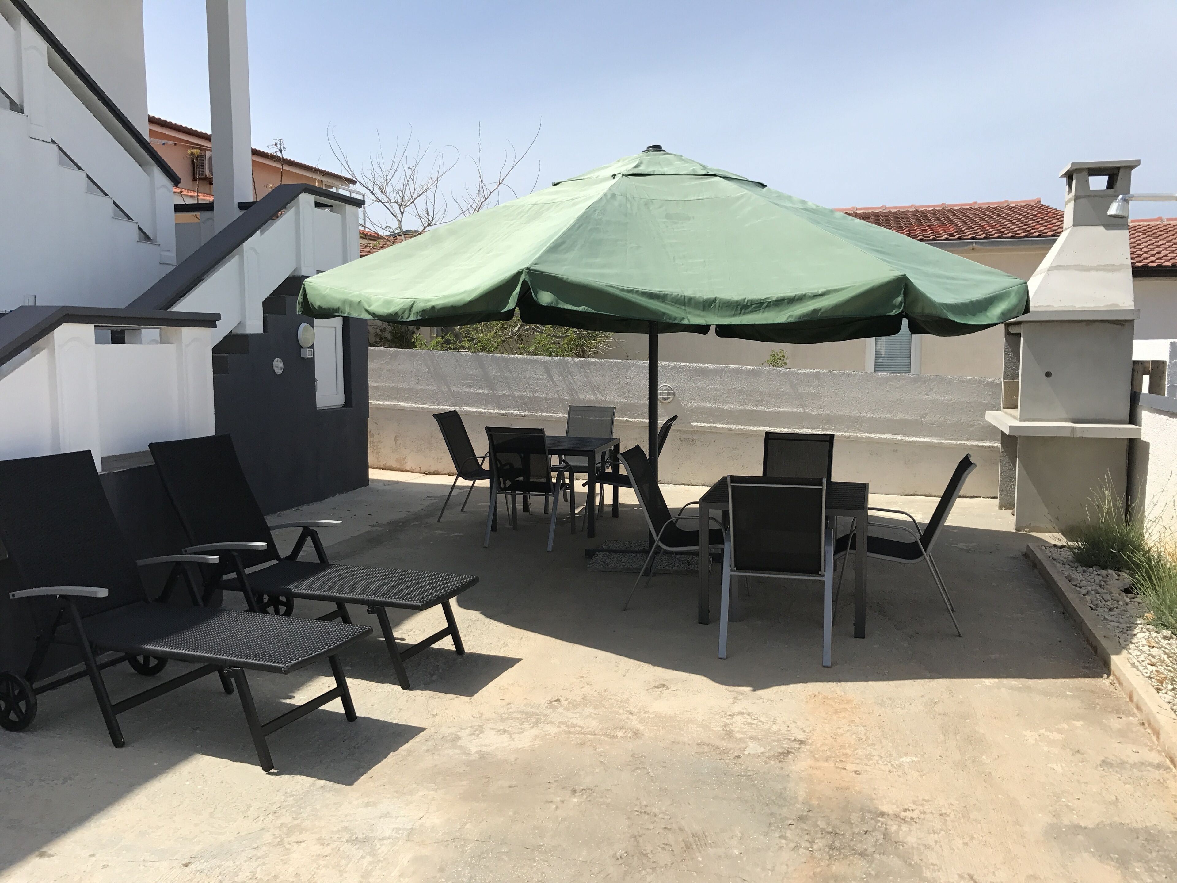 Eine Terrasse im Freien mit einem grünen Sonnenschirm, schwarzen Stühlen und einem Grill.