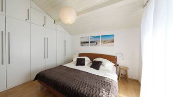 A bedroom with a bed, wooden floor, white wardrobe, and a hanging light fixture.