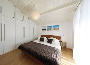 A bedroom with a bed, wooden floor, white wardrobe, and a hanging light fixture.