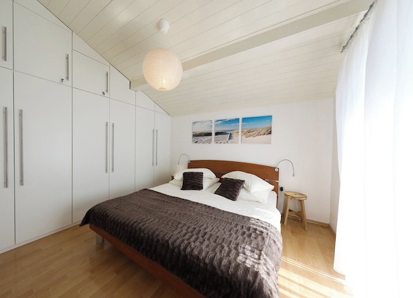 A bedroom with a bed, wooden floor, white wardrobe, and a hanging light fixture. - Apartment Josip (VIR)