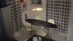 A compact kitchen with a dining table, chairs, a refrigerator, and a hanging light fixture.