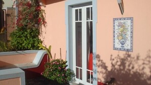 A building with a white door, a small garden area with pink flowers, and a tiled wall with a floral design.