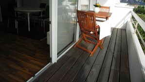 Une terrasse en bois avec une table et des chaises, une porte-fenêtre coulissante et une rambarde blanche.