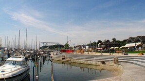 Un port de plaisance avec des bateaux amarrés, une promenade piétonne et des bâtiments en arrière-plan.