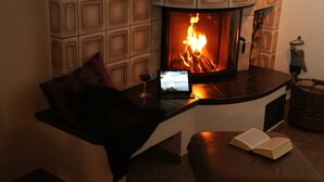 Una habitación acogedora con chimenea, una computadora portátil, una copa de vino y un libro abierto sobre una mesa.