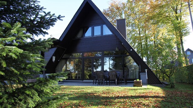Una casa moderna de forma triangular con amplios ventanales y una zona de comedor con mobiliario exterior.