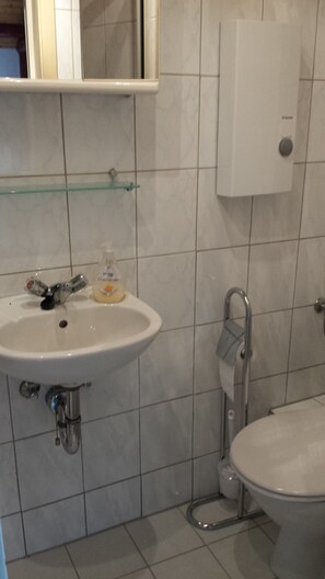 Ein Badezimmer mit Waschbecken, Spiegel, Seifenspender, Toilette und Handtuchhalter.