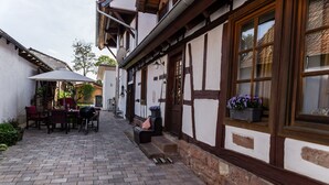 Un edificio tradicional con entramado de madera, un patio de ladrillo, asientos al aire libre y una ventana con flores.