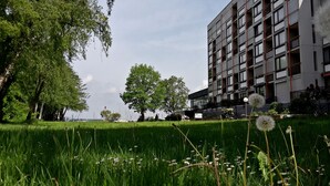Un edificio moderno con varios pisos y balcones, rodeado de abundante vegetación y un césped cuidado.