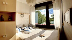 Un dormitorio con una cama grande, una ventana con vistas a árboles, una estantería y un armario.