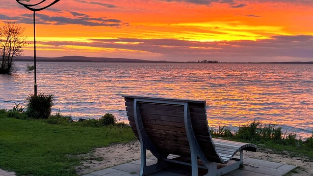 Un banco junto a la orilla de un lago al atardecer.