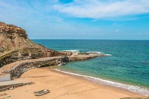 A coastal beach with a rocky cliff, a sandy shore, and a small boat. - CASA DO MAR - HOUSE BY THE SEA - (Areia Branca/ Ortsteil Casal Labrusque)