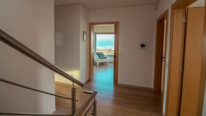 A modern interior with a wooden staircase, a view of the ocean through an open door, and a white chair in the background.