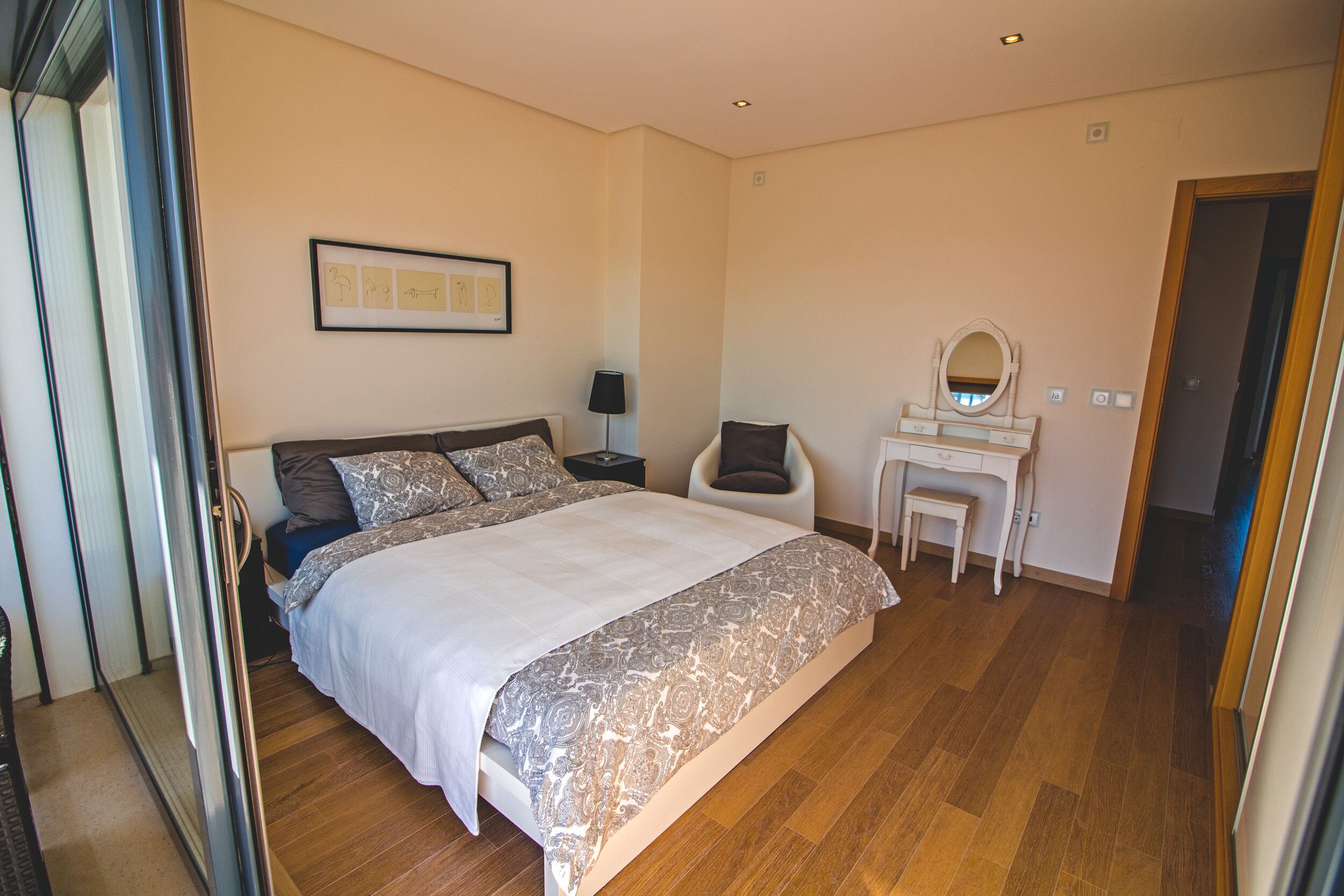 Een slaapkamer met een groot bed, een nachtkastje, een stoel, een bureau en een spiegel.
