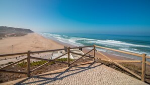 A beach with a wooden staircase leading down to the shore, a paved walkway, and a clear view of the ocean.
