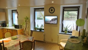 Un coin repas avec une table dressée pour deux personnes, un téléviseur fixé au mur et des plantes en pot.