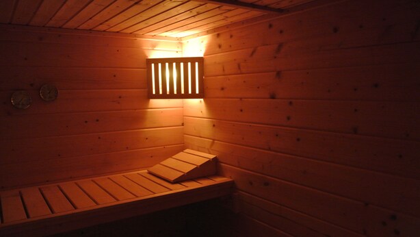 Un sauna en bois avec un banc, un radiateur fixé au mur et deux horloges murales.