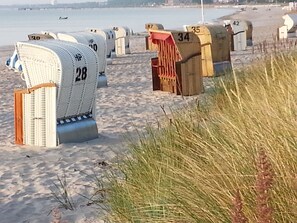 A row of numbered beach huts on a sandy beach with a body of water in the background. - Sunrises and ocean sounds inclusive (Scharbeutz)