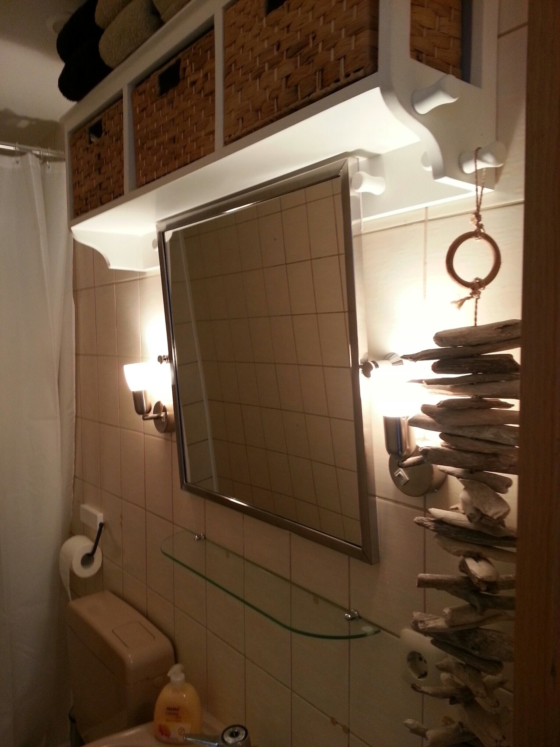 A bathroom with a tiled wall, a mirror, a toilet, a glass shelf, and a towel rack.